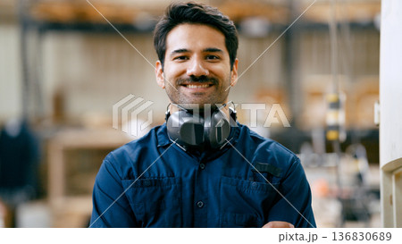 Carpenter smiling, wearing hearing protection in workshop 136830689