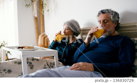 Senior couple enjoying healthy breakfast and orange juice in bed Senior couple enjoying healthy breakfast and orange juice in bed 136830729