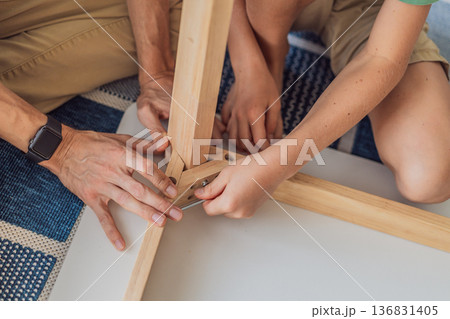 Father and his son assembling a table together in the living room at home. Meaningful family moment showing teamwork, learning and support. Fatherhood, home improvement and bonding through shared Father and his son assembling a table together in the living room at home. Meaningful family moment showing teamwork, learning and support. Fatherhood, home improvement and bonding through shared 136831405