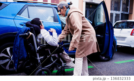 Caregiver helping person with reduced mobility getting into car Caregiver helping person with reduced mobility getting into car 136832333