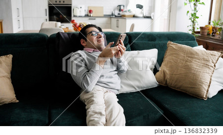 Man with spina bifida smiling on sofa using smartphone Man with spina bifida smiling on sofa using smartphone 136832339
