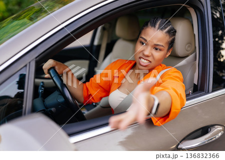Young black woman driving car and gesturing with hand out of window Young black woman driving car and gesturing with hand out of window 136832366
