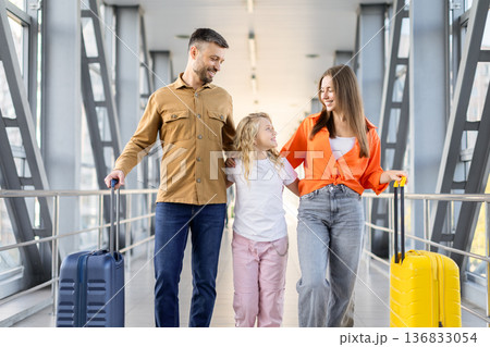 Parents walking with daughter at airport terminal, smiling and enjoying family holiday 136833054