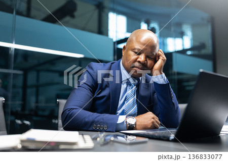 Bored black businessman leaning on hand while working on laptop in office 136833077