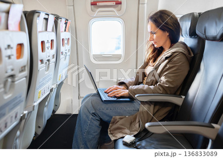 Female passenger working on laptop inside airplane cabin during flight 136833089