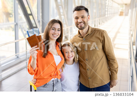 Happy family of three holding passports while standing at airport terminal Happy family of three holding passports while standing at airport terminal 136833104