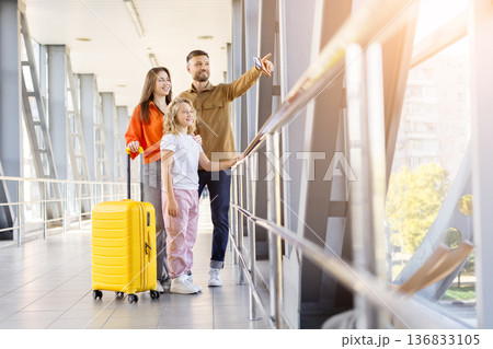 Happy family standing at airport terminal and looking through window 136833105