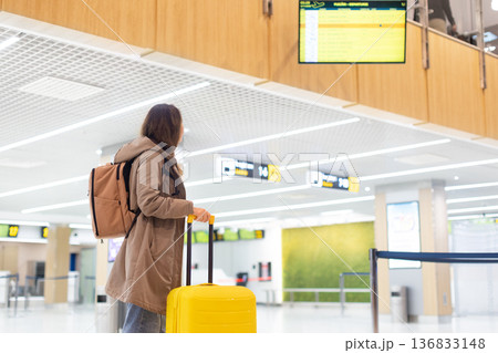 Adult woman with backpack and suitcase checking flight information board in airport Adult woman with backpack and suitcase checking flight information board in airport 136833148