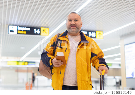 Adult caucasian male traveler walking in airport terminal with passport and luggage Adult caucasian male traveler walking in airport terminal with passport and luggage 136833149