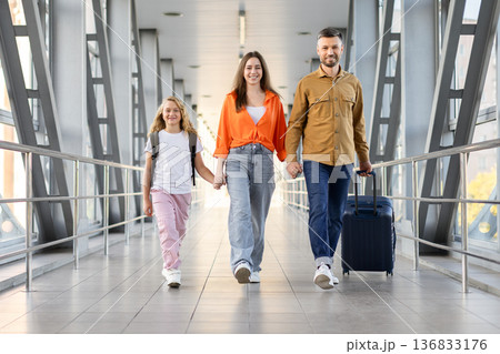 Smiling caucasian family walking through airport terminal with luggage, holding hands 136833176