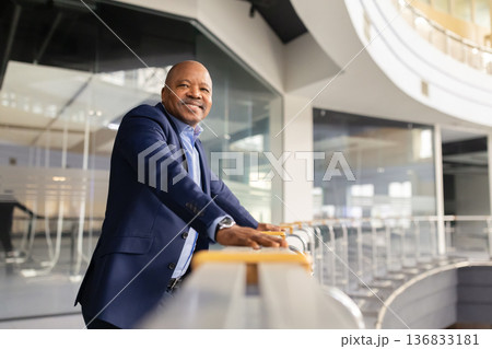 Mature black businessman leaning on balcony railing in office building and smiling 136833181