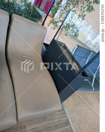 Leather lounge chairs are arranged in the lounge area of Valencia Airport. Travelers can use these chairs while they wait for their flights. Greenery adds to the atmosphere. 136834250