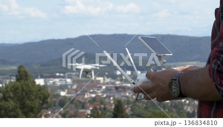 Person operates a drone above a city in the daytime with hills in the background 136834810
