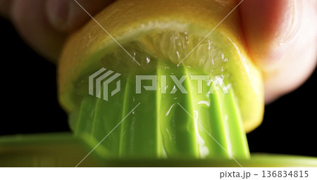 Juice is being extracted from a lemon using a green juicer in a kitchen setting during the day 136834815