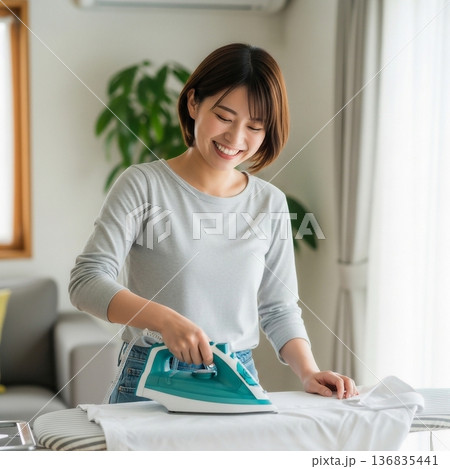 居間でアイロン台を使って衣服にアイロンをかける若い女性 居間でアイロン台を使って衣服にアイロンをかける若い女性 136835441