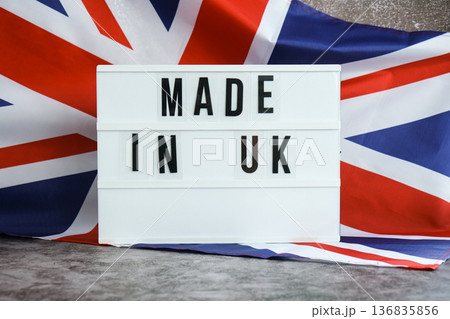 Letter board with message MADE IN UK National symbol of Great Britain. British wave silky flag background. Pride product quality standard and reliability Letter board with message MADE IN UK National symbol of Great Britain. British wave silky flag background. Pride product quality standard and reliability 136835856