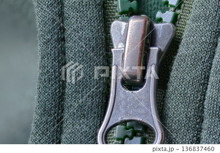 Detailed view of green plastic zipper teeth and metal slider on a textured green garment Detailed view of green plastic zipper teeth and metal slider on a textured green garment 136837460