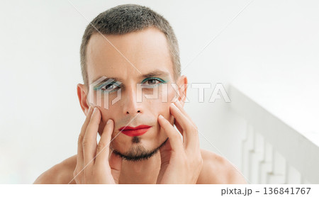 portrait of gay man with makeup and cosmetics on his face. A handsome young transgender male with red lipstick on lips and mascara on eyes on a white background portrait of gay man with makeup and cosmetics on his face. A handsome young transgender male with red lipstick on lips and mascara on eyes on a white background 136841767