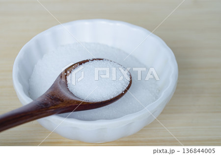 White salt poured into small ceramic bowl with wooden spoon illustrating everyday cooking ingredient. 136844005