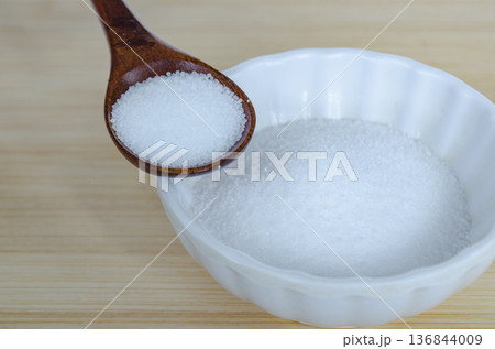 Wooden spoon filled with white salt placed on ceramic bowl over light wooden background representing sodium intake and dietary health awareness concept. Health concept. Wooden spoon filled with white salt placed on ceramic bowl over light wooden background representing sodium intake and dietary health awareness concept. Health concept. 136844009