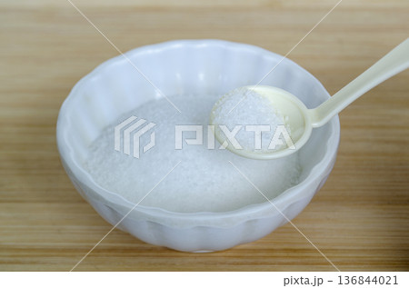 White ceramic spoon scooping salt from bowl highlighting sodium measurement and nutritional balance in daily meals. White ceramic spoon scooping salt from bowl highlighting sodium measurement and nutritional balance in daily meals. 136844021