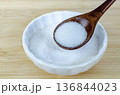 Close up of granulated sugar in wooden spoon placed in white bowl highlighting sweetener use and diabetes risk consideration. 136844023