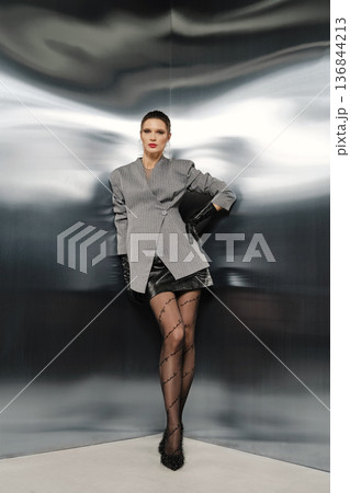 Model poses in stylish outfit against reflective background at a fashion event Model poses in stylish outfit against reflective background at a fashion event 136844213