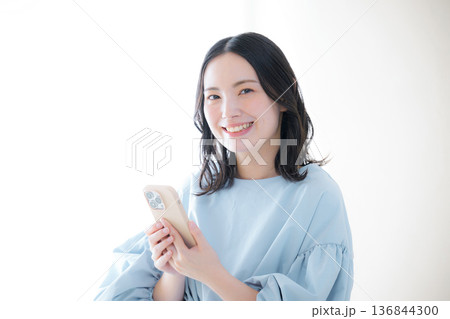 スマホを操作する笑顔の女性 カメラ目線　オンライン利用・サービスなどの口コミ 136844300