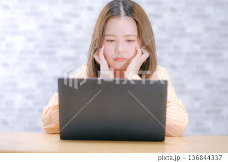 ノートパソコンを見ながら悩む20代日本人女性 ノートパソコンを見ながら悩む20代日本人女性 136844337