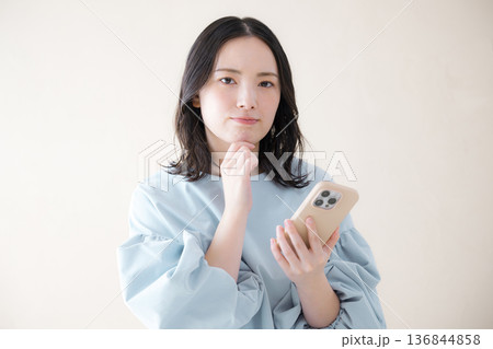 スマホを操作する女性 　オンライン利用・サービスなどの検索、スマホを見る困る悩む顎に手を当てるポーズ 136844858