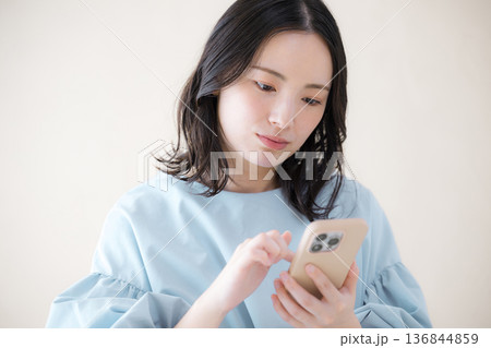 スマホを操作する女性 　オンライン利用・サービスなどの検索、スマホを見る困る悩む顎に手を当てるポーズ 136844859
