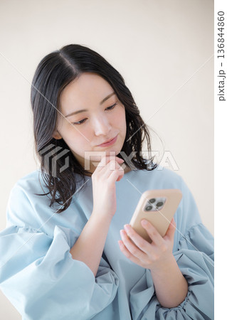 スマホを操作する女性 オンライン利用・サービスなどの検索、スマホを見る困る悩む顎に手を当てるポーズ スマホを操作する女性 オンライン利用・サービスなどの検索、スマホを見る困る悩む顎に手を当てるポーズ 136844860