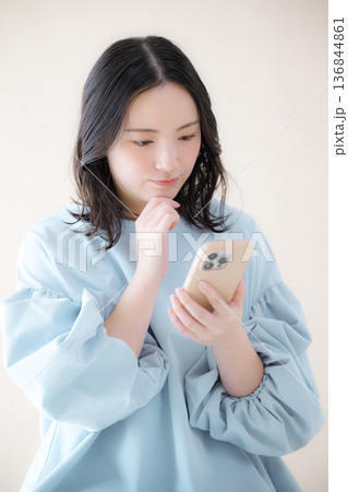スマホを操作する女性 　オンライン利用・サービスなどの検索、スマホを見る困る悩む顎に手を当てるポーズ 136844861