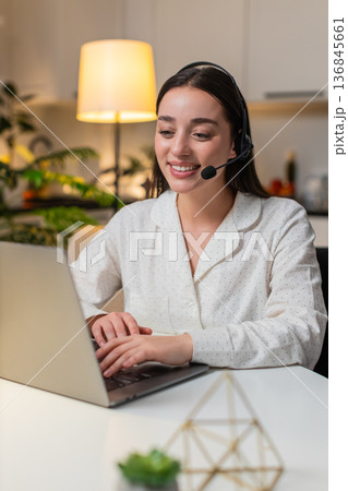 Young woman with headset answers hotline support call logs customer ticket polite operator evening Young woman with headset answers hotline support call logs customer ticket polite operator evening 136845661