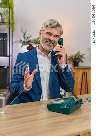 Middle-aged businessman smiles nostalgically speaking on retro cord phone from 90s during work break 136845664