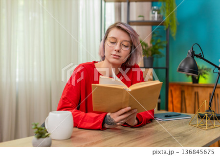 Young woman thoughtfully reading book turning pages concentrated serious expression literature hobby 136845675