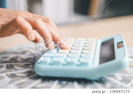 Close-up of a hand pressing calculator keys for budgeting, accounting and financial analysis. Business expense planning, tax calculation, office desk background, copy space for paperwork. 136847173