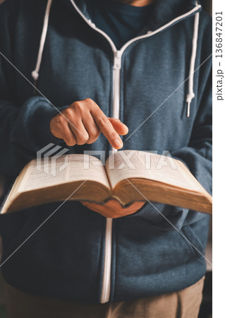 Man holding an open Bible and turning pages, warm indoor light and shallow depth of field, symbolizing Christian faith, devotion, scripture study and quiet worship at home. Man holding an open Bible and turning pages, warm indoor light and shallow depth of field, symbolizing Christian faith, devotion, scripture study and quiet worship at home. 136847201