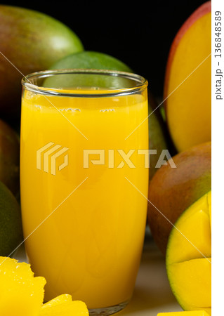 Glass of fresh mango juice surrounded by whole and sliced fruits. Glass of fresh mango juice surrounded by whole and sliced fruits. 136848589