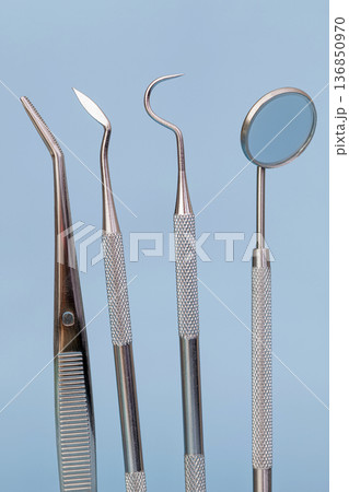 Close-up of dental instruments set with mirror, scaler and explorer on blue background, vertical medical dentistry concept Close-up of dental instruments set with mirror, scaler and explorer on blue background, vertical medical dentistry concept 136850970