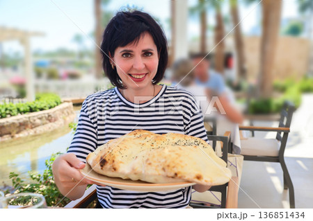 A woman holds a huge, fluffy Turkish bread on a tray 136851434