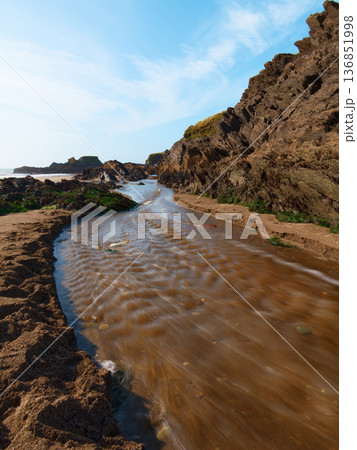 Coastal stream flows across golden sand to meet the crashing ocean waves under a blue sky. Coastal stream flows across golden sand to meet the crashing ocean waves under a blue sky. 136851998