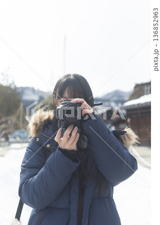 雪の街並みでカメラを構える女性　冬の旅スナップ 136852963