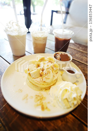 Fresh Iced coffee with gorgeous pancakes topped with banana and chocolate ice cream with whipped cream and butter in white plate on wooden table Fresh Iced coffee with gorgeous pancakes topped with banana and chocolate ice cream with whipped cream and butter in white plate on wooden table 136853447