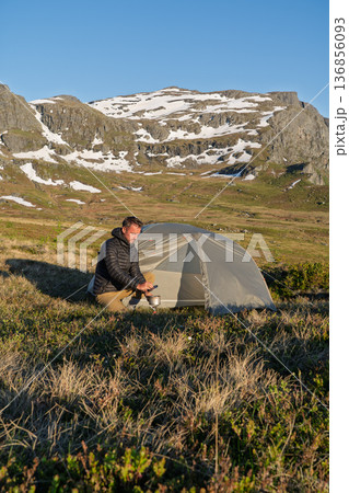 Male hiker cooking at wild camp in mountains above Hardangerfjord, Norway 136856093