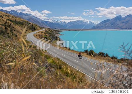 Wide view of cyclist on scenic road to Mount Cook by Lake Pukaki, NZ 136856101