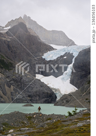Hiker standing by Laguna Los Perros below massive glacier, Patagonia, Chile 136856103