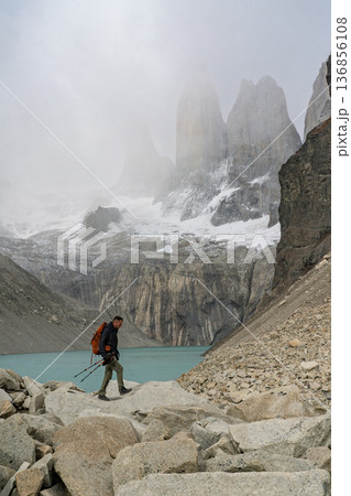 Hiker navigating rocky terrain below misty Torres del Paine, Patagonia 136856108