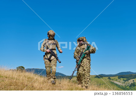Two Soldiers in Camouflage Patrol Hillside With Sniper and Infantry Rifle During Military Training Two Soldiers in Camouflage Patrol Hillside With Sniper and Infantry Rifle During Military Training 136856553
