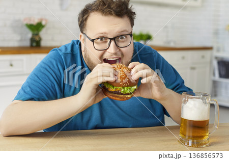 Plus-size man enjoying burger and beer at home kitchen, cheat meal concept 136856573